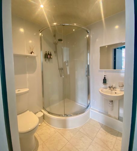 Compact bathroom featuring a shower, toilet, and small basin. Brightly lit with modern fixtures.