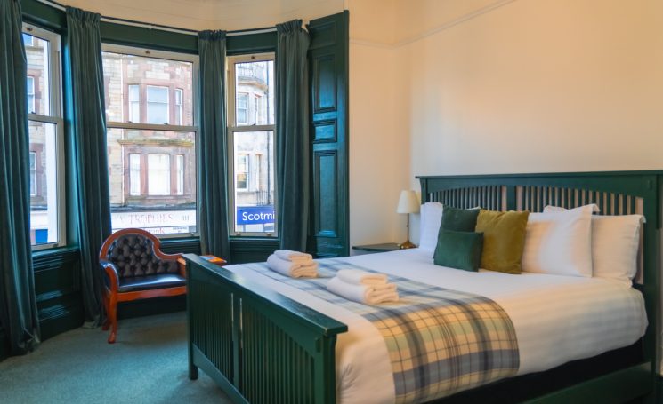 A spacious bedroom with a double bed, chair, and large windows with green curtains.